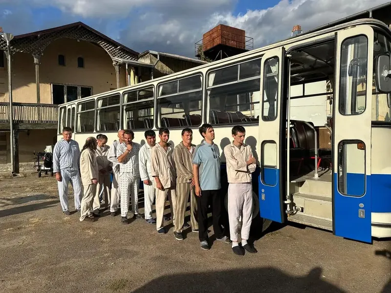 Figuranți în costum, aliniați lângă un autobuz de epocă, pe platoul de filmare