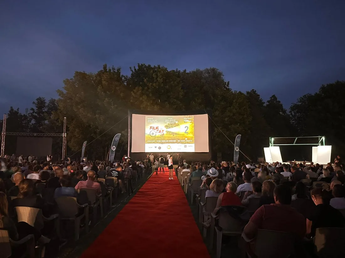 Covor roșu și public numeros la o proiecție de cinema în aer liber, în amurg