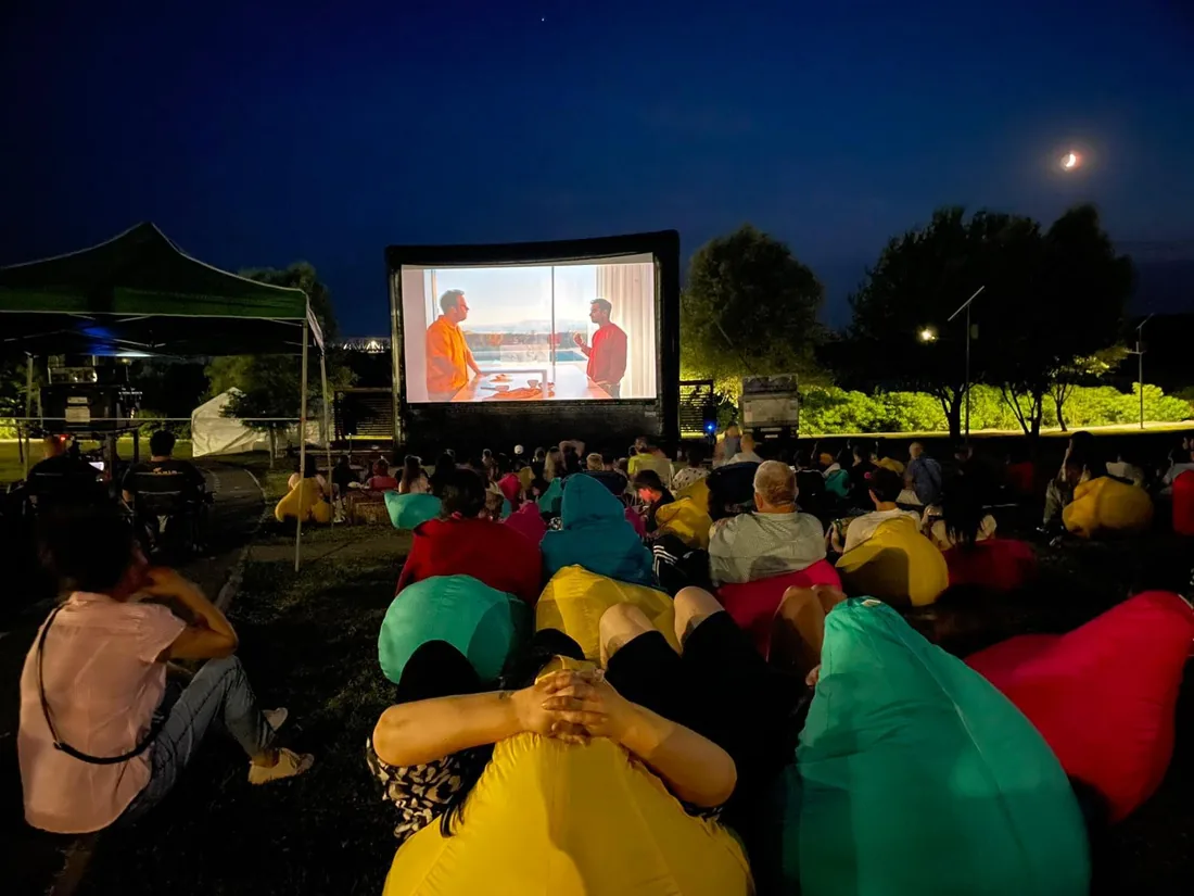 Public pe puf-uri colorate, la o proiecție de cinema în aer liber, noaptea